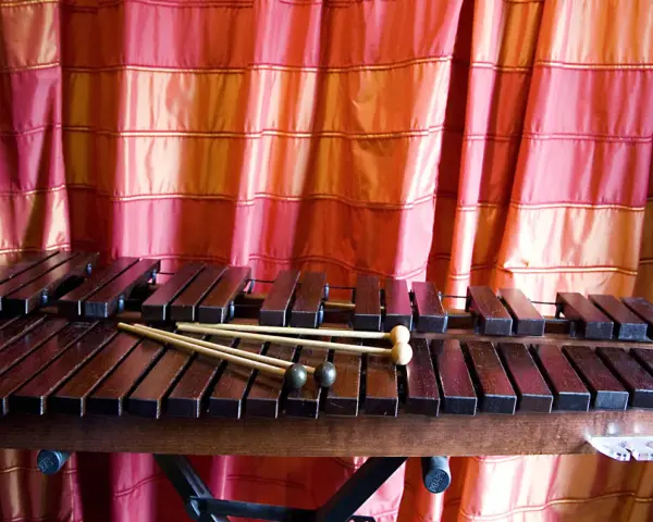 Ksylofon, instrument muzyczny na literę K, z pałeczkami, na tle czerwonej zasłony.