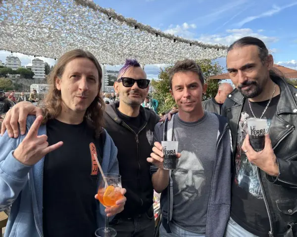 Quatre hommes, un groupe hollandais des années 80, posent avec des boissons. L'un fait un signe de rock.