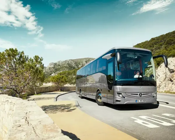 Srebrny Mercedes Tourismo jedzie malowniczą trasą nad morzem.