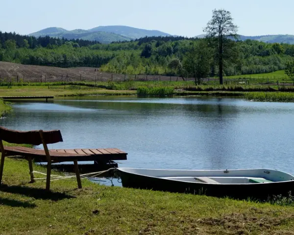 Idealne miejsce na camping nad stawami: łódka przy pomoście, ławka i spokojna tafla wody.