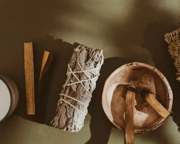 Palo santo kadzidło właściwości: świeca, biała szałwia, miseczka z drewienkami palo santo i bukiety ziół.