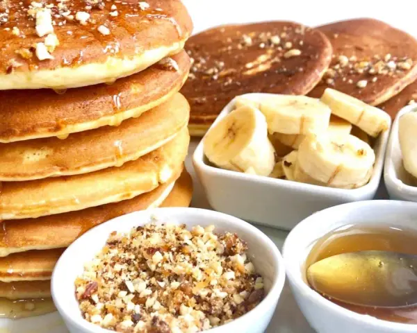 Pile de pancakes dorés arrosés de miel, accompagnés de rondelles de banane, de noix concassées et d'une cuillère de miel. Un délice pour le petit-déjeuner !