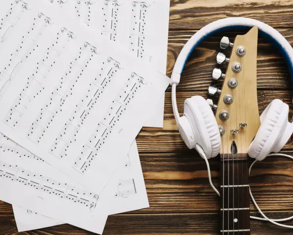 Nuty i gitara z białymi słuchawkami. Idealne do tego, by znaleźć piosenkę po nuceniu i stworzyć własną melodię.