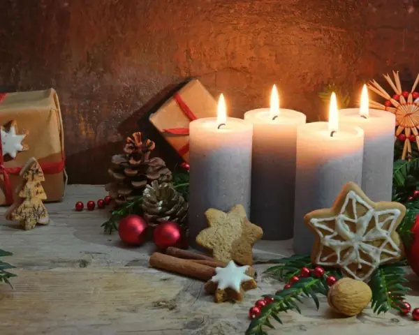 Vier brennende Kerzen im **Hintergrund Adventszeit**, umgeben von Tannenzweigen, Geschenken, Nüssen und Weihnachtsplätzchen.