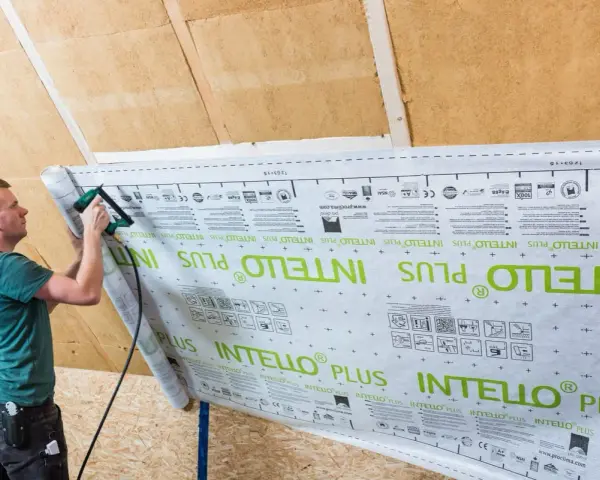 Mann bringt mit einem Tacker eine Dampfbremse an. Die Folie ist mit "INTELLO PLUS" bedruckt.