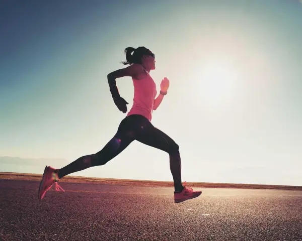 Donna corre su strada asfaltata al tramonto, con il sole che illumina la scena. Questo è un esempio di tempo run, un allenamento per migliorare la velocità.