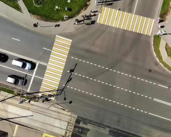 Vista aerea di un incrocio con strisce pedonali bianche e gialle. Auto in attesa nella corsia di preselezione, tram sui binari sottostanti.