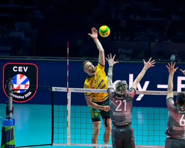 Emocjonujący moment w final ligi mistrzów siatkówka. Zawodnik w żółtej koszulce atakuje, a dwaj gracze w szarych strojach próbują go zablokować.