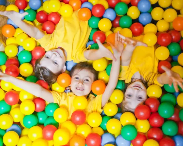 Drei Kinder in gelben T-Shirts spielen in einem Bällebad. Perfekte Ausflugsziele mit Kindern für Spaß und Lachen.