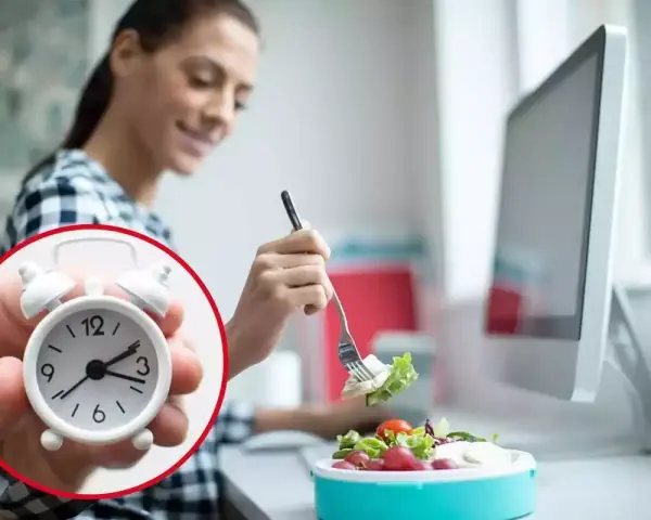 Mujer comiendo ensalada en su escritorio, con un reloj que marca el tiempo para comer en el trabajo.