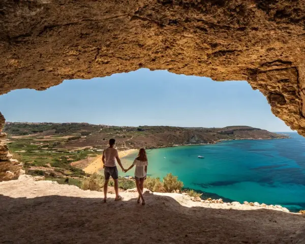 Para zakochanych podziwia widok na turkusowe morze i plażę z jaskini. Malta w styczniu pogoda idealna na spacer.