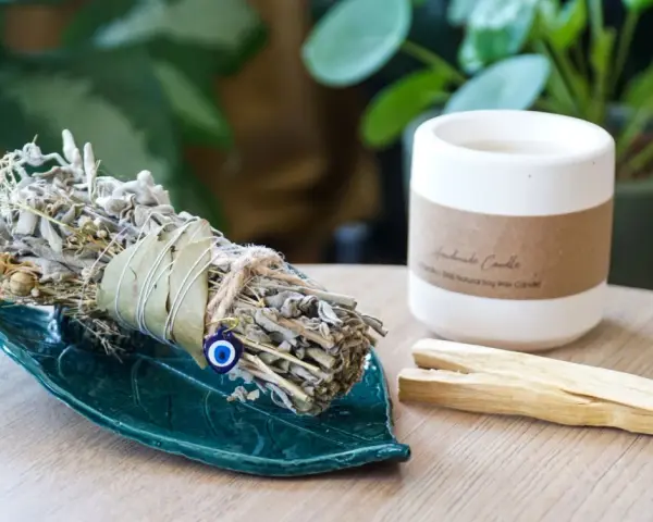 Ziołowe kadzidło na zielonej podstawce, obok świeca i patyczki palo santo. Idealne do rytuału, jak zrobić kadzidło.