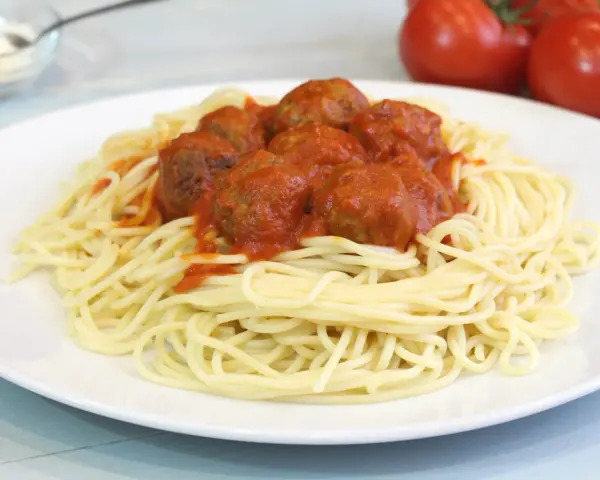 Un plato de espaguetis con albóndigas cubiertos de salsa roja.