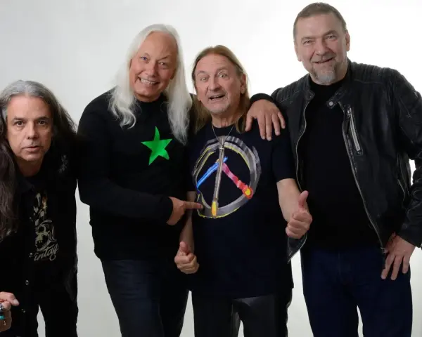 Czterech mężczyzn, TSA Dream Team, pozuje do zdjęcia. Dwóch z nich ma długie włosy, jeden w czarnej koszulce z zieloną gwiazdą, drugi w koszulce z symbolem pokoju.