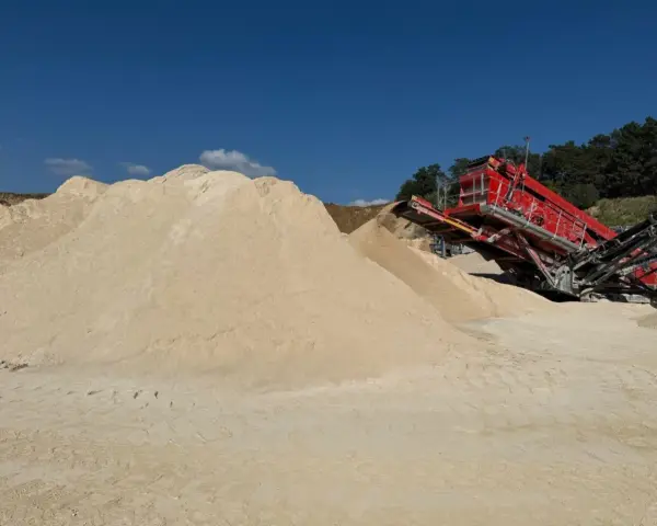 Góra piasku, prawdopodobnie wapno węglanowe, obok czerwonej maszyny do przesiewania na placu budowy.