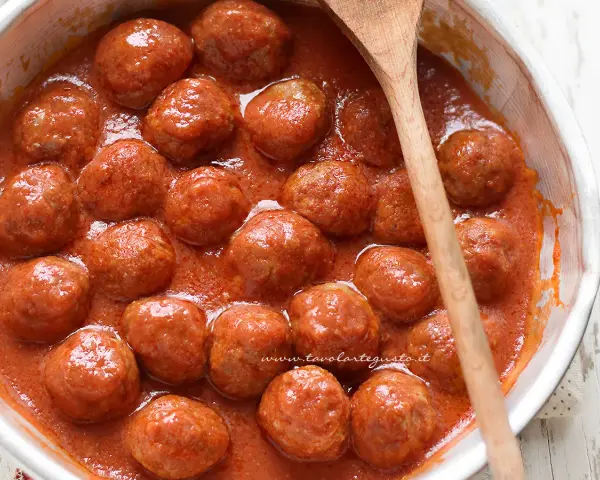 Polpette al sugo fumanti in una ciotola, pronte per essere gustate. Un cucchiaio di legno le accompagna.