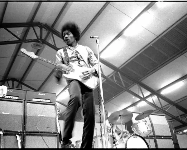 Jimi Hendrix, icône du jimi hendrix style de musique, électrise la scène avec sa guitare blanche. Amplis Marshall et batterie en arrière-plan.