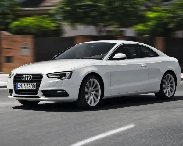 Białe Audi A5 Coupe pędzi po drodze, jego sylwetka jest dynamiczna i elegancka.
