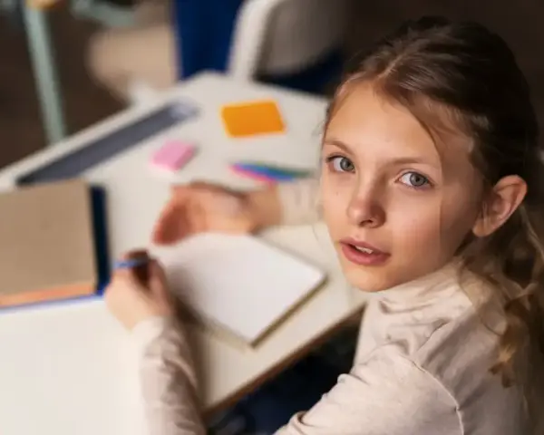 Dziewczynka zmagająca się z dysleksją rozwojową próbuje pisać w zeszycie, patrząc z nadzieją na pomoc.