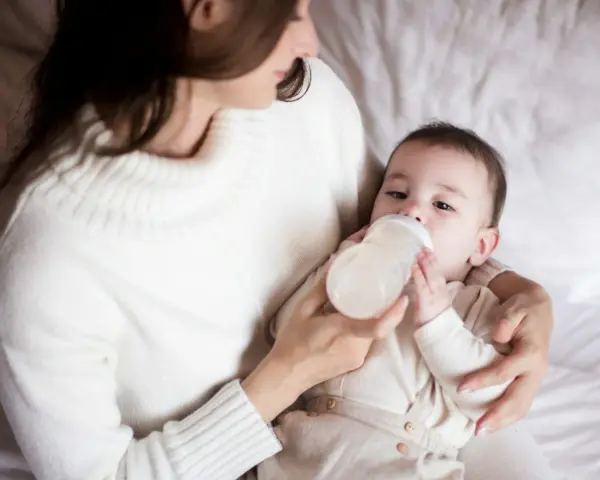 Mama karmi butelką dziecko, które właśnie pije mleko. Ważne jest, ile mleka powinien jeść noworodek.