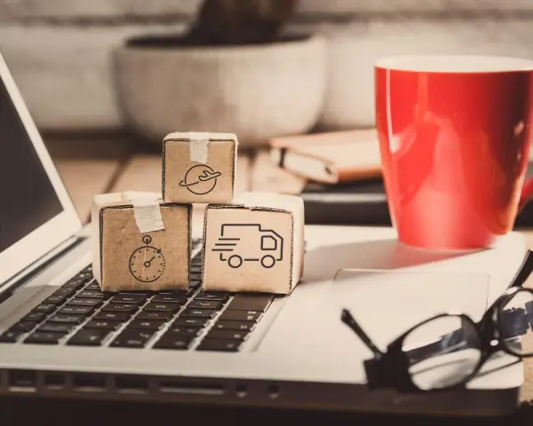 Miniaturki paczek z ikonami transportu na klawiaturze laptopa. Zastanawiasz się, ile zarabia spedytor?