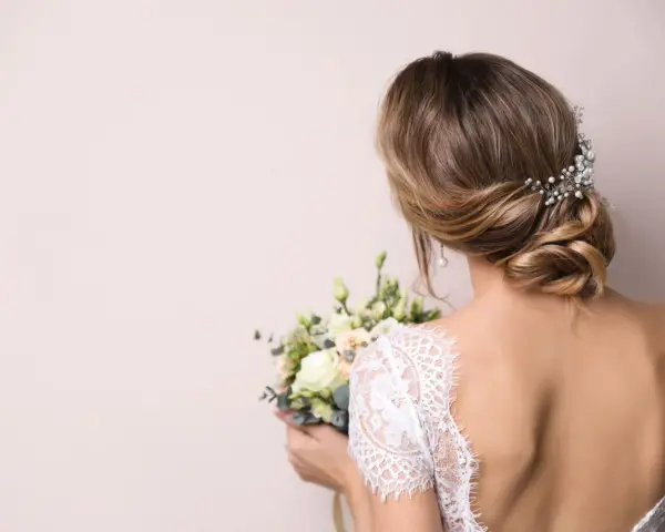 Eleganckie wesele: wlosy podpiete z jednej strony, ozdobione perłami, z bukietem kwiatów w dłoni.