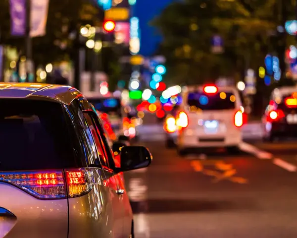 Luci sfocate e colorate in una strada trafficata di notte, come vedono i miopi le luci. Un'auto argentata in primo piano.