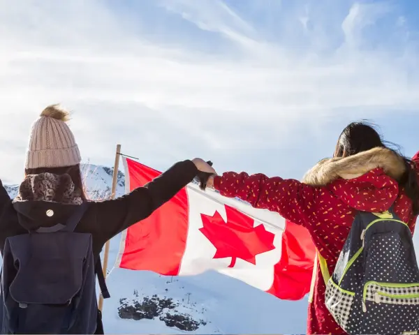 Zwei junge Frauen mit Rucksäcken und der kanadischen Flagge in den Bergen. Ein unvergesslicher Kanada Austausch!