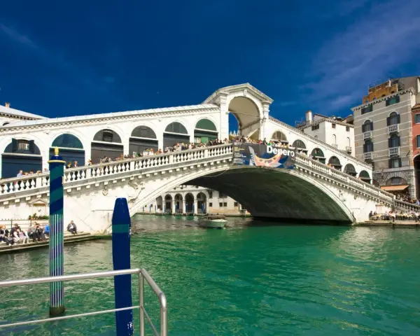 Ponte di Rialto, un'icona della storia veneziana, con le sue botteghe e la folla che lo attraversa, si specchia nelle acque verdi del Canal Grande.