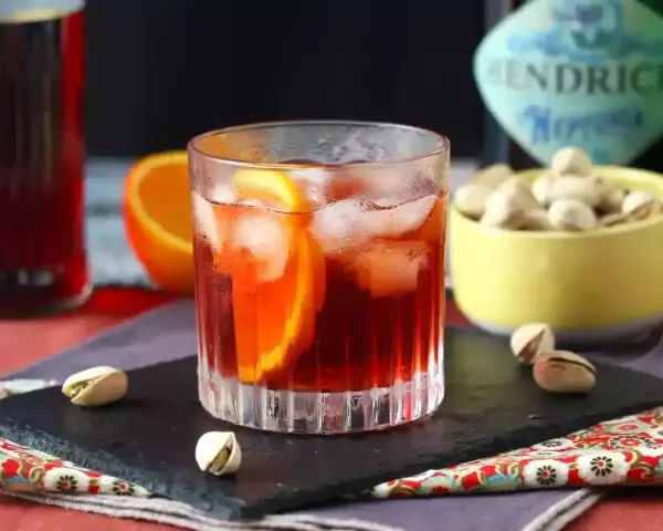 Przepis na Negroni Sbagliato: orzeźwiający drink z pomarańczą i lodem, obok miseczka pistacji.