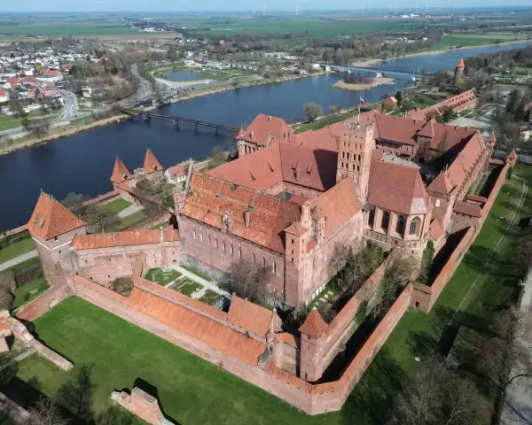 Potężny zamek z czerwonej cegły, największy zamek w Europie, otoczony murami obronnymi, nad rzeką.