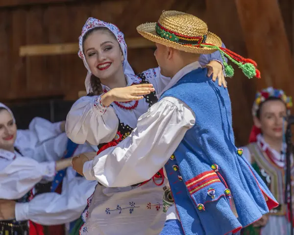 Uśmiechnięta para w tradycyjnych strojach tańczy do skocznych piosenek ludowych.