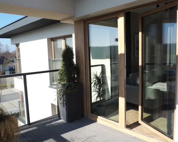 Nowoczesny balkon z drewnianymi, podwójnymi drzwiami balkonowymi. Okna dzielone poziomo wpuszczają dużo światła.