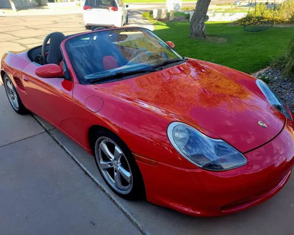 Roter Porsche Boxster Cabriolet. Die glänzende Karosserie spiegelt den Himmel wider. Ein Blick auf die potenziellen Porsche Service Kosten.