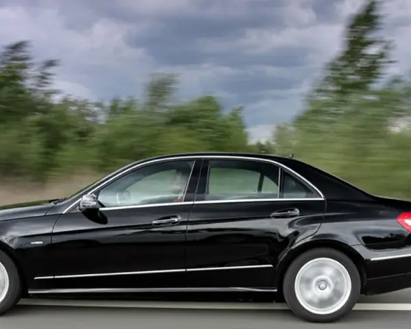 Czarny Mercedes E350 pędzi po drodze, mijając rozmyte zielone drzewa.