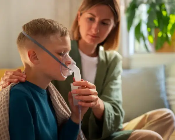 Chłopiec z maską nebulizatora, wspierany przez matkę. Dbałość o zdrowie dziecka z astmą wczesnodziecięcą.