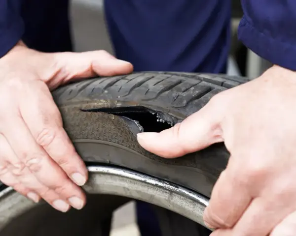 Dłonie mechanika badają oponę po głośnym wystrzale. Widoczne jest duże rozdarcie bieżnika.