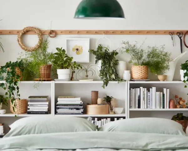 Grüne Pflanzen im Schlafzimmer schaffen eine beruhigende Atmosphäre. Auf weißen Regalen stehen diverse Pflanzen in Körben und Töpfen, daneben Bücher und Deko.