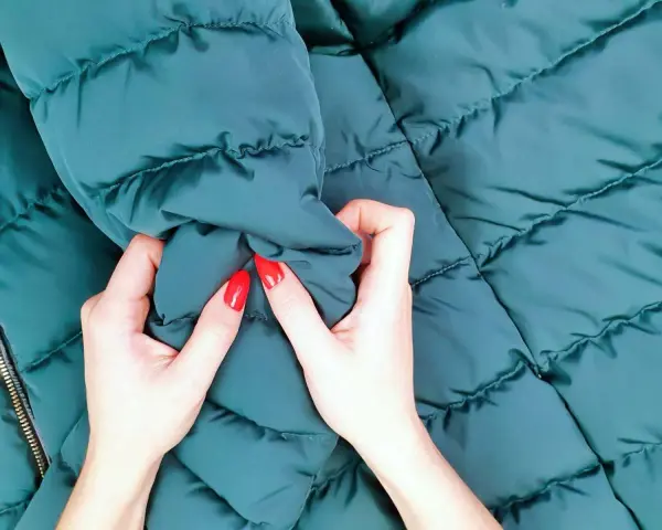 Manos con uñas rojas arrugan una chaqueta verde oscuro. ¡Por fin he lavado un plumas en la lavadora y está como nuevo!