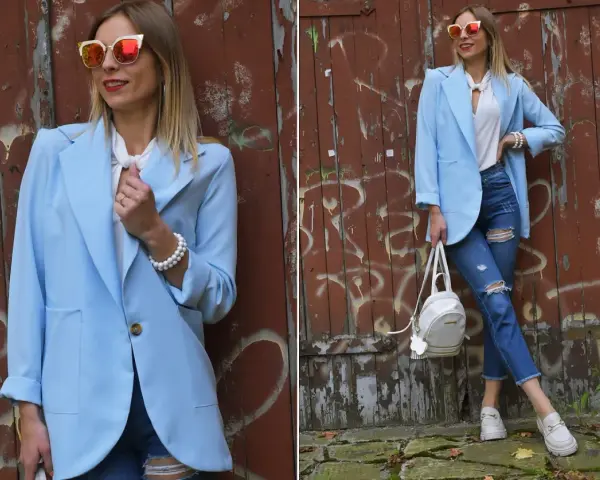 Kobieta w błękitnej marynarce i podartych jeansach prezentuje stylowe stylizacje. Okulary przeciwsłoneczne dodają charakteru.