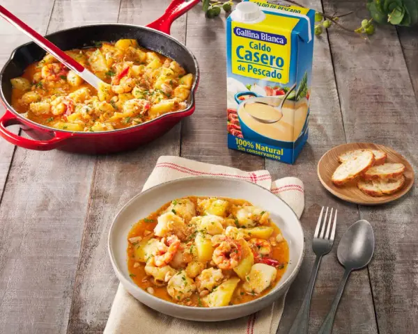Un delicioso rape a la marinera, con patatas y gambas, servido en una cazuela roja y un plato.