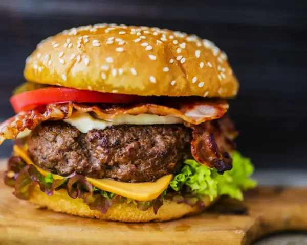 Hamburger di carne succulento con bacon croccante, formaggio fuso, pomodoro e lattuga su panino ai semi di sesamo.
