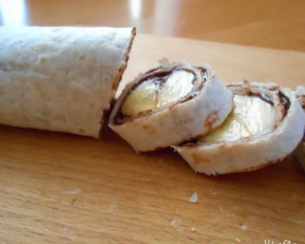 Słodka tortilla z bananem i czekoladą, pokrojona w rolki, wygląda jak pyszny deser.