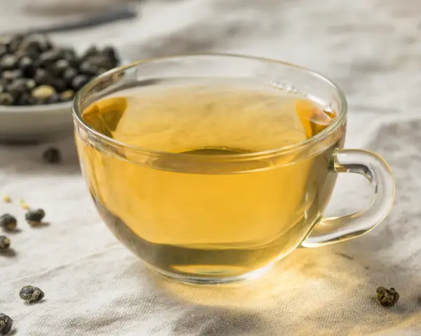 Zaparzona herbata oolong w szklance, obok miseczka z suszonymi liśćmi. Odkryj niezwykłe herbata oolong właściwości.