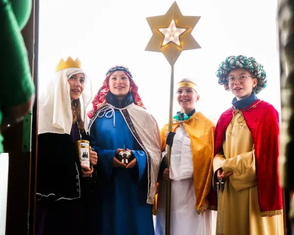 Vier Kinder als Sternsinger evangelisch verkleidet, mit Stern und Spendenbüchse, stehen vor einer Tür.