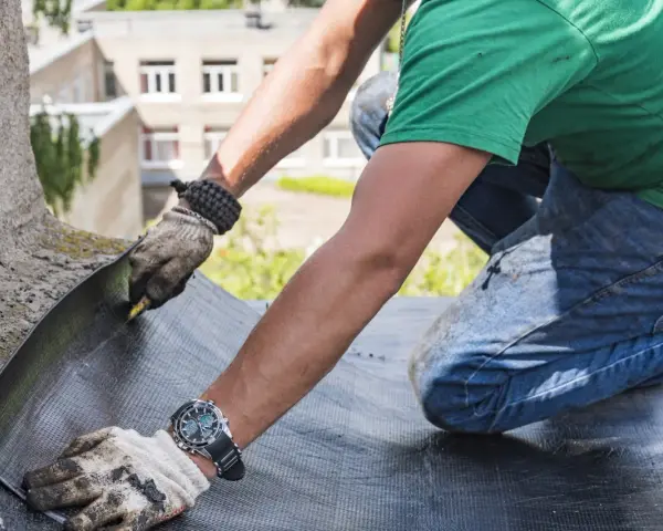 Trabajador realiza impermeabilización de terrazas, cortando material para asegurar la protección contra el agua.