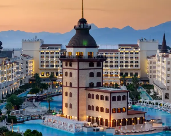 Luksusowy hotel z basenami i wieżą, idealny na wakacje all inclusive w Turcji. Góry w tle.