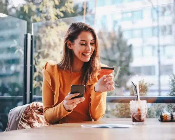 Smiling woman uses phone and credit card. She's researching if you need an LLC for a business credit card.