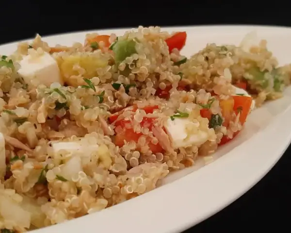 Salade colorée de quinoa avec des dés de feta, avocat, tomates et persil, servie dans un plat blanc.