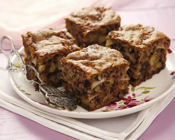 Vier Stücke saftiger Apfel Walnuss Kuchen auf einem Teller mit Blumenmuster, daneben ein antiker Tortenheber.